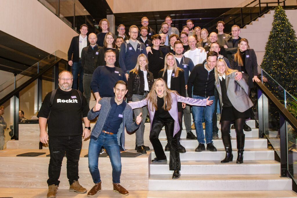 Large group photo of FIRSTPICK Accelerator Batch 3 cohort standing together on a staircase, smiling and celebrating at an event. The group includes startup founders, mentors, and team members in a lively atmosphere with a decorated Christmas tree in the background.